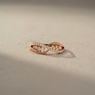 Front view of an infinity diamond ring in 14 KT Rose Gold, featuring intertwining crossover bands accented with pavé-set and floating round lab-grown diamonds in an elegant openwork design, displayed against a beige backdrop