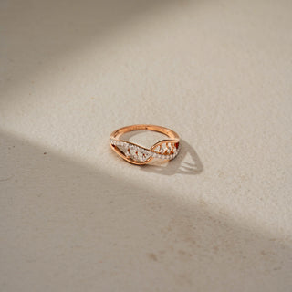 Top view of an infinity diamond ring in 14 KT Rose Gold, featuring intertwining crossover bands accented with pavé-set and floating round lab-grown diamonds in an elegant openwork design, displayed against a beige backdrop
