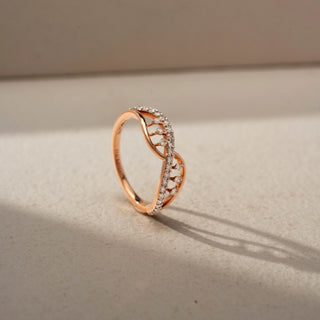 Angled view of an infinity diamond ring in 14 KT Rose Gold, featuring intertwining crossover bands accented with pavé-set and floating round lab-grown diamonds in an elegant openwork design, displayed against a beige backdrop