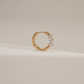 Close-up of petite three-stone diamond nose ring in 14KT Yellow Gold, placed on a neutral surface, showcasing EF-VVS round diamonds in a sleek circular push-and-pull design.