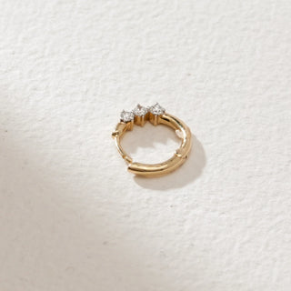 Overhead view of petite three-stone diamond nose ring in 14KT yellow gold, placed on a textured white surface, featuring EF-VVS round diamonds in a minimal circular design.