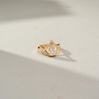 Top view of a yellow gold ring featuring a pear-cut diamond center framed by a pavé diamond chevron design, accented with a graceful twisted band for a modern, elegant look.