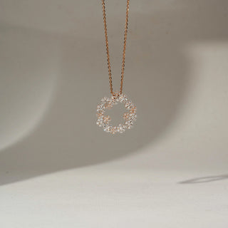 Front-facing view of a rose gold necklace with an open floral wreath pendant, featuring clustered sparkling diamonds suspended on a fine chain against a soft neutral background.