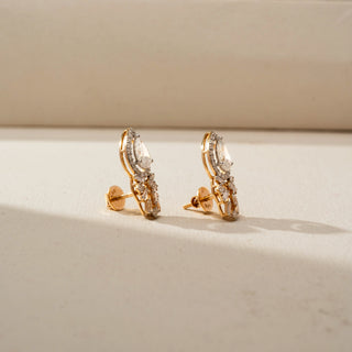 Side view of pear-shaped halo diamond earrings with floral-inspired clusters of round and baguette diamonds, showcasing the profile, settings, and screw-back posts on a softly lit surface.