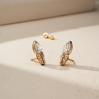 Angled view of pear-shaped halo diamond earrings with floral-inspired clusters of round and baguette diamonds, showcasing the side profile, settings, and screw-back posts on a softly lit surface.