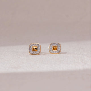 Front view of square halo stud earrings in yellow gold, featuring a central yellow stone surrounded by round lab-grown diamonds. Placed on a soft beige surface, the design reflects bold geometric elegance.
