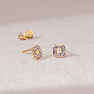 Top view of square halo stud earrings in yellow gold, featuring an open centre framed by round lab-grown diamonds. Placed on a textured beige surface, the design casts a soft shadow.
