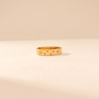 Front view of a 14KT yellow gold ring featuring floral diamond motifs and star accents, set against a beige background.
