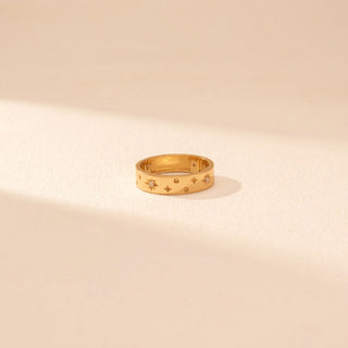 Top view of a 14KT yellow gold ring featuring floral diamond motifs and star accents, set against a beige background.