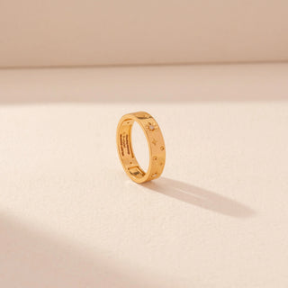 Angled view of a 14KT yellow gold ring featuring floral diamond motifs and star accents, set against a beige background.