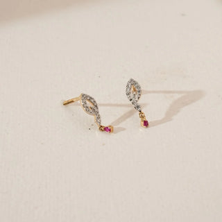 Angled view of marquise-shaped diamond earrings with pavé-set lab grown diamonds and small ruby drop accents in yellow gold, displayed on a soft neutral surface.