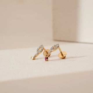 Side view of marquise-shaped diamond earrings with pavé-set lab grown diamonds and small ruby drop accents in yellow gold, displayed on a soft neutral surface.