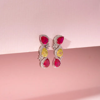 Close up view of ruby, yellow sapphire and lab-grown  round cut diamond drop earrings in 14 KT rose gold, featuring pear-shaped ruby and yellow sapphire gemstones framed by pavé-set diamond halos with floral diamond accents.