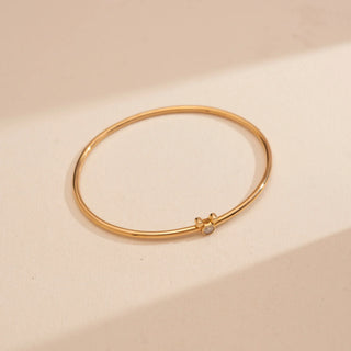 Top-down view of Reia’s 14 KT Yellow Gold Charming Diamond Mouse Bangle. Captured on a cream backdrop, it highlights the smooth, high-polish finish of the gold surface.