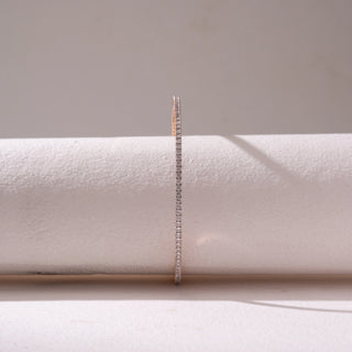 Front view of a slim diamond tennis bracelet in Rose gold, featuring a continuous row of pavé-set diamonds. Captured against a soft beige backdrop, the design reflects refined sparkle and elegance.
