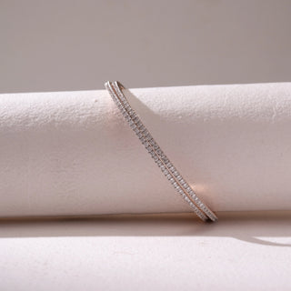 Angled view of a slim diamond tennis bracelet in Rose gold, featuring double rows of pavé-set diamonds. Captured against a soft beige backdrop, the design reflects refined sparkle and elegance.
