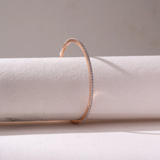Side view of a slim diamond bangle in Rose gold, featuring a single row of pavé-set diamonds. Captured against a soft beige backdrop, the design reflects refined sparkle and minimal elegance.

