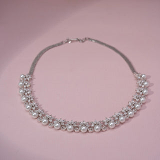 Top view of a pearl and lab-grown diamond necklace in 14KT White Gold, featuring round pearls with floral diamond motifs. Captured against a pink backdrop, the elegant design blends classic charm with radiant sparkle.