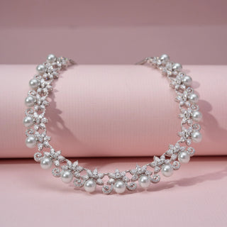 Angled view of a pearl and lab-grown diamond necklace in 14KT White Gold, featuring round pearls with floral diamond motifs. Captured against a pink backdrop, the intricate design radiates timeless elegance.