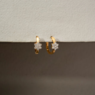Side view of floral diamond hoop earrings in 18 KT Yellow Gold, featuring sparkling flower-shaped diamond clusters set on sleek gold hoops against a neutral backdrop.
