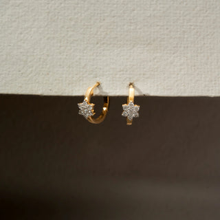 Angle view of floral diamond hoop earrings in 18 KT Yellow Gold, featuring sparkling flower-shaped diamond clusters set on sleek gold hoops against a neutral backdrop.
