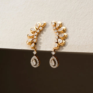 Angled view of diamond ear climber earrings in 14 KT Yellow Gold, featuring pear-shaped diamonds in a graceful curved arrangement with dangling pear halo drops against a neutral backdrop.
