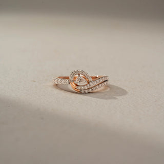 Front view of a swirl diamond ring in 14 KT Rose Gold, featuring a floating round lab-grown diamond framed by intertwining pavé-set diamond bands in an elegant crossover design, displayed against a beige backdrop.