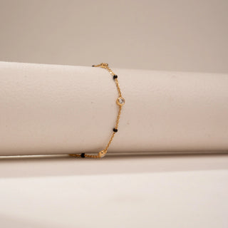 Side view of a 14KT Yellow Gold bracelet with chain links, black beads and round bezel-set diamond stations.