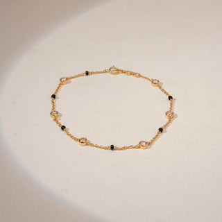 Top view of a 14KT Yellow Gold bracelet with chain links, black beads and round bezel-set diamond stations.