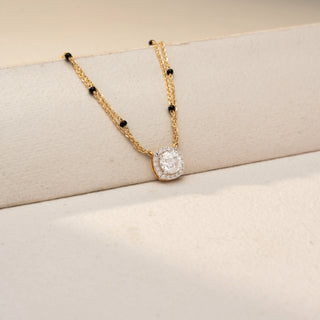 Angled view of a diamond halo mangalsutra necklace in 14 KT Yellow Gold, featuring a round lab-grown diamond encircled by a sparkling halo, suspended from a double-chain design with black bead accents, displayed on a beige backdrop.