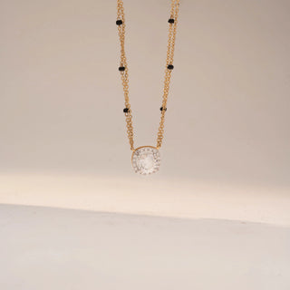 Front view of a diamond halo mangalsutra necklace in 14 KT Yellow Gold, featuring a round lab-grown diamond encircled by a sparkling halo, suspended from a double-chain design with black bead accents, displayed on a beige backdrop.