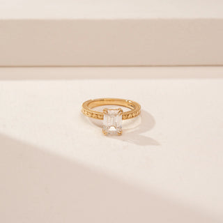 Close up view of a 14KT Yellow Gold diamond ring, featuring an emerald-cut centre diamond and textured band.