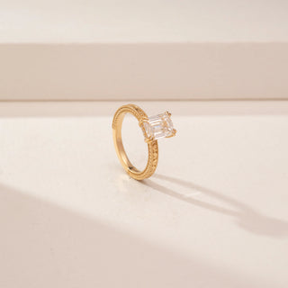Angled view of a 14KT Yellow Gold diamond ring, featuring an emerald-cut centre diamond and textured band.