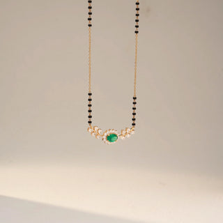 Side view of a yellow gold lab-grown diamond mangalsutra featuring an oval emerald centre gemstone with a halo and leaf-inspired diamond accents on a classic black bead chain, displayed on a neutral background.