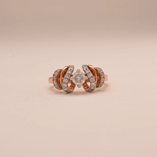 Front view of Reia’s 14 KT Rose Gold Radiant Curve Diamond Designer Ring. The centred round diamond is framed by fluid, diamond-set curves on a rose gold band against a soft pink surface.