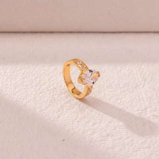 Side view of oval diamond ring in yellow gold, featuring a centred oval lab-grown diamond with channel-set side stones on a wide band. Placed on a textured beige surface, the design casts a soft shadow.
