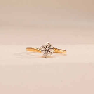 Front view of Reia’s 14 KT Yellow Gold Timeless Single Stone Diamond Ring. It features a brilliant round diamond in a minimal setting with a sleek, curved band against a clean, cream backdrop.