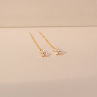 Side view of a 14KT yellow gold earrings featuring floral diamond details with delicate chain drops, set against a beige background.