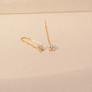 Angled view of a 14KT yellow gold earrings featuring floral diamond details with delicate chain drops, set against a beige background.