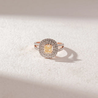 Top view of Cushion Halo Diamond Ring in 14KT Rose Gold, featuring a central cushion-cut yellow diamond surrounded by layered pavé halos and a split diamond band. Set on a soft beige surface, it exudes brilliance.
