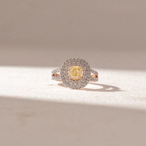 Front view of Halo Cushion Diamond Ring in 14KT Rose Gold, featuring a central cushion-cut yellow diamond encircled by double halo pavé diamonds. Set on a soft beige surface, the design radiates brilliance and elegance.