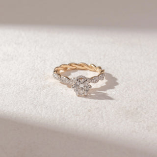 Top view of round diamond solitaire ring in yellow gold with a twisted pavé band, set on a soft neutral surface, highlighting braided detail and bright, radiant sparkle.
