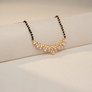 Angled view of a floral diamond mangalsutra necklace in 14 KT Dual Gold, featuring pear-shaped lab-grown diamonds arranged in cascading floral clusters, accented by black beads and displayed on a beige backdrop.