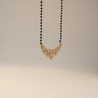 Side view of a floral diamond mangalsutra necklace in 14 KT Dual Gold, featuring pear-shaped lab-grown diamonds arranged in cascading floral clusters, accented by black beads and displayed on a beige backdrop.