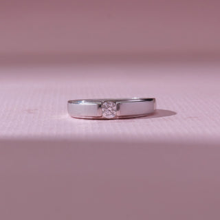 Front view of a sleek diamond ring in white gold, featuring a centred round-cut diamond set between polished flat bands. Captured on a soft pink backdrop, highlighting modern minimalism.
