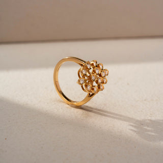 Angled view of a floral diamond statement ring in 14 KT Yellow Gold, featuring round lab-grown diamonds arranged in an intricate fan-shaped floral motif with openwork detailing, displayed against a beige backdrop.