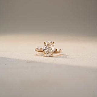 Front view of an oval three-stone ring in 14 KT Yellow Gold, featuring a central oval-cut lab-grown diamond flanked by tapered baguette diamonds, displayed against a beige backdrop.