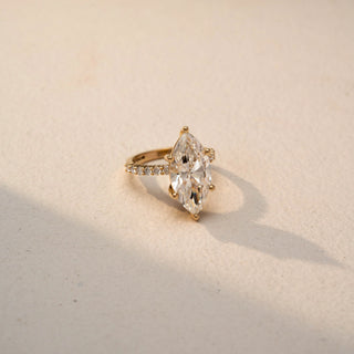 Side view of a marquise diamond engagement ring in 14 KT Yellow Gold, featuring a marquise-cut lab-grown diamond with pavé-set diamonds along the band, displayed against a beige backdrop.

