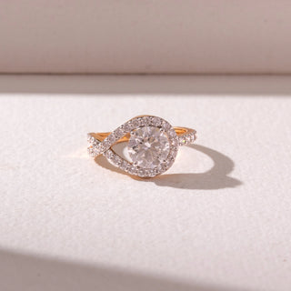 Top view of a yellow gold diamond halo ring, featuring a round center stone framed by a pavé swirl design. Captured against a soft beige backdrop, the design reflects graceful sparkle and elegance.
