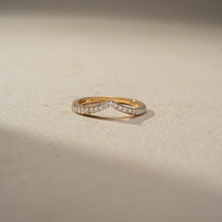 Front view of a curved diamond wedding band in 14 KT Yellow Gold, featuring a chevron-shaped silhouette adorned with pavé-set round lab-grown diamonds, displayed against a beige backdrop.